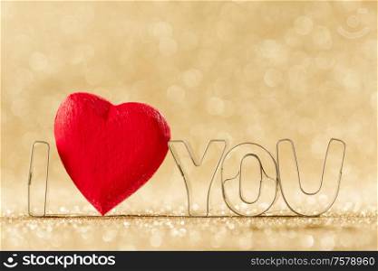 Red handmade wooden heart in I LOVE YOU sign word on golden bright glitter lights bokeh background. Wooden heart and I LOVE YOU