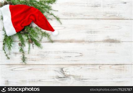 Red hat with green pine tree branches on bright wooden background. Christmas decoration