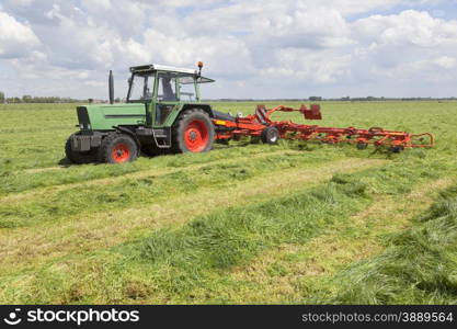 red hay turner behind tractor in green meadow in the netherlands