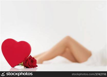 red heart and a wet red rose in front of beautiful legs from a woman
