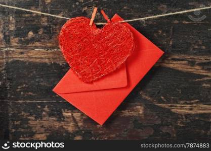 Red heart and envelop hanging on the clothesline. On old wood background