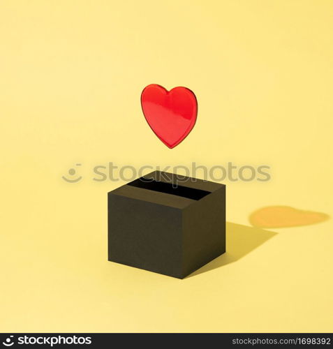 Red heart comes out of a black box and floats on a yellow background. Valentine&rsquo;s Day. Abstract. Square layout with copy space.. a red heart comes out of a black box and floats on a yellow background. Valentine&rsquo;s Day.