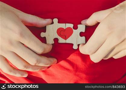 Red heart is drawn on the pieces of the puzzle in male hands on red background. Love concept. People Relations. St. Valentine day. Red heart is drawn on the pieces of the puzzle in male hands on red background. Love concept. St. Valentine day