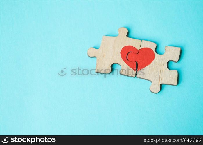 Red heart is drawn on the pieces of the wooden puzzle lying next to each other on blue background. Love concept. St. Valentine day. Reconciliation. Reunion concept. Free space for text. Red heart is drawn on the pieces of the wooden puzzle lying next to each other on blue background. Love concept. St. Valentine day. Copy space.