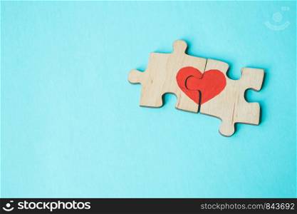 Red heart is drawn on the pieces of the wooden puzzle lying next to each other on blue background. Love concept. St. Valentine day. Reconciliation. Reunion concept. Free space for text. Red heart is drawn on the pieces of the wooden puzzle lying next to each other on blue background. Love concept. St. Valentine day. Copy space.