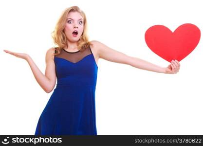 Red heart. Love symbol. Surprised woman hold Valentine day symbol and showing empty hand palm with copyspace for product or text. Cute blonde girl in blue dress expressing tender feelings. Isolated studio shot