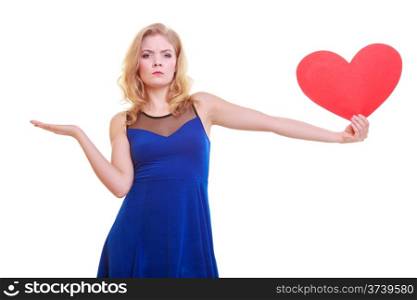 Red heart. Love symbol. Woman hold Valentine day symbol and showing empty hand palm with copyspace for product or text. Unhappy angry blonde girl in blue dress expressing tender feelings. Isolated studio shot