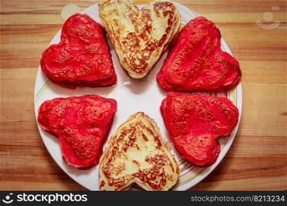 Red heart shaped pancakes made with love for valentines day and tulips on wooden background