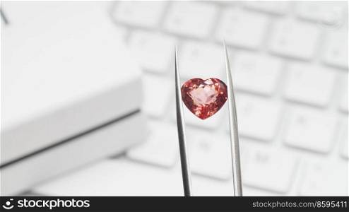 Red heart shaped tourmaline gem in tweezers. Online jewelry shopping for birthday, Valentine Day, other holiday. Gemologist or jeweller holding red tourmaline, macro shot with box and keyboard. Online jewelry shopping with heart shaped tourmaline