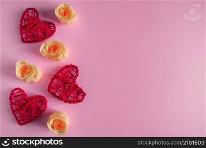 Red hearts and orange rosebuds on a pink background. Concept for Valentine&rsquo;s Day. Place for text.. Red hearts and rosebuds on a pink background, concept for Valentine&rsquo;s Day.