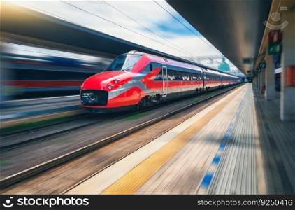 Red high speed train in motion on the railway station. Fast moving modern intercity train and blurred background. Railway platform. Railroad in Italy. Commercial and passenger railway transportation 