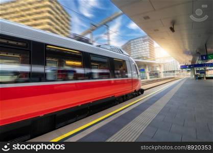 Red high speed train in motion on the railway station at sunset. Fast modern intercity train and blurred background. Railway platform. Railroad in Austria. Commercial and passenger transportation