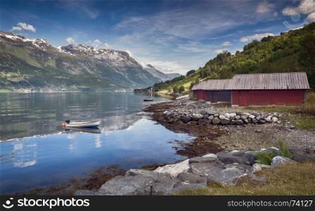 red houses and a boat in the fjord in norway with mountains as background