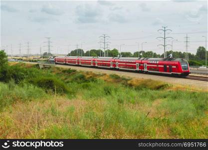 Red israeli passenger train in motion out of the city near Highway 4.