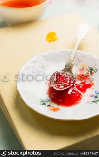 Red jam in vintage spoon and plate on a book, close up, still life