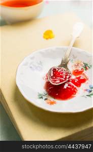 Red jam in vintage spoon and plate on a book, close up, still life