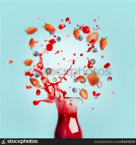 Red juice or smoothie drink is poured out of glass bottle with splash and berries ingredients on turquoise background, front view. Healthy summer beverage concept