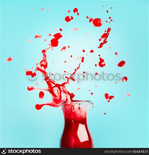 Red juice or smoothie glass bottle with splash on turquoise background, front view. Healthy summer beverage concept