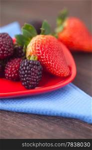 red juicy strawberry and blackberry in red plate on a wooden surface