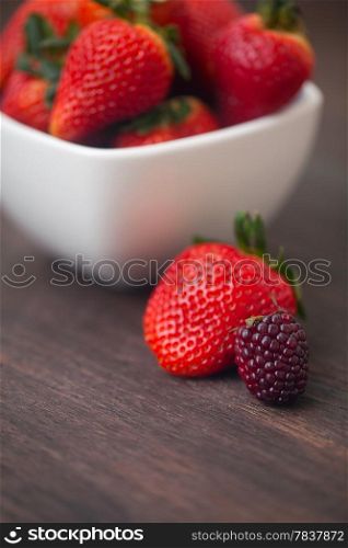 red juicy strawberry in a bowl and blackberry on a wooden surface