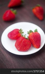 red juicy strawberry in a plate on a wooden surface