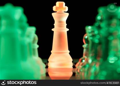 red king and rows of green glass chess pieces is standing on board in dark