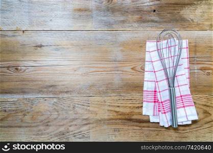 Red kitchen towel with whisk on a wood wood background.. Red kitchen towel with whisk on a wood wood background