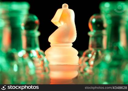 red knight and rows of green glass chess pieces is standing on board in dark