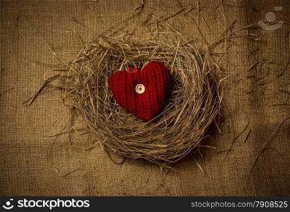 Red knitted decorative heart lying in birds nest on linen cloth