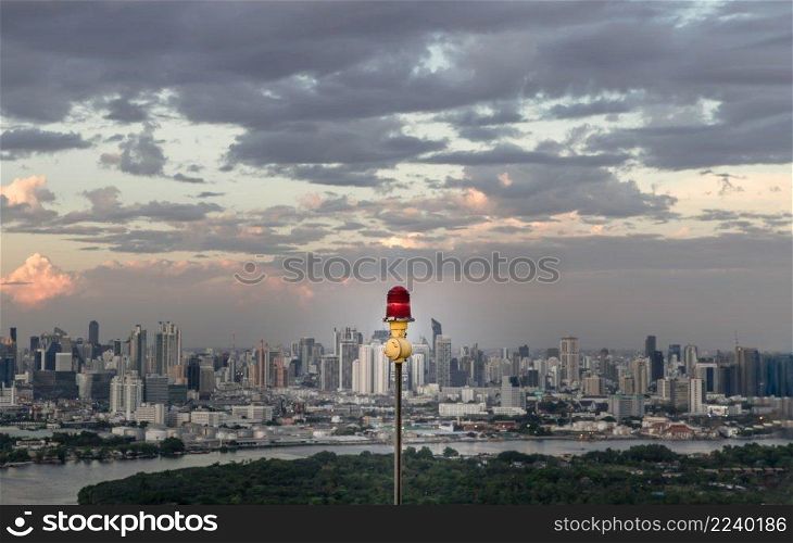 Red lantern of obstruction lights mounted on the rooftop of high rise tall building to ensure flights safety and warn the danger for the plane on the city view background at sunset. Red alarm l&, Selective focus.