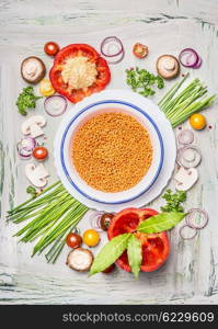 Red lentil in bowl and vegetables ingredients for healthy vegetarian cooking, top view composing.