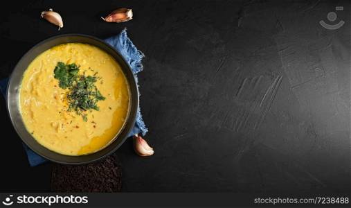 Red lentil soup, spices, herbs, vegetables, lemon and cream. Soup on a blue napkin, next to garlic cloves. Black background, top view. Copy space for text.