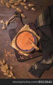 Red lentils in a ceramic bowl with a wooden scoop on a kitchen countertop.