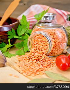 Red lentils in a glass jar, parsley, garlic, tomatoes, clay pot, napkin on the background of wooden boards