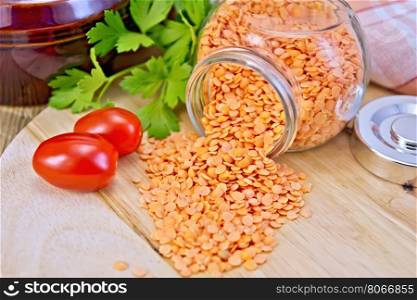 Red Lentils in a glass jar, parsley, tomatoes, a clay pot and napkin on a wooden boards background