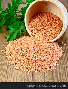 Red lentils in a wooden bowl with green parsley on a wooden boards background