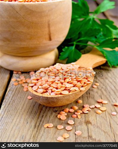 Red lentils in a wooden spoon and a bowl on a wooden boards background