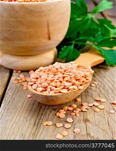 Red lentils in a wooden spoon and a bowl on a wooden boards background