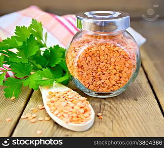 Red lentils in a wooden spoon and a glass jar, parsley, napkin on wooden board