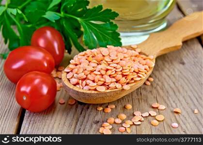 Red lentils in a wooden spoon, tomatoes, parsley, vegetable oil in a carafe on the background of wooden boards