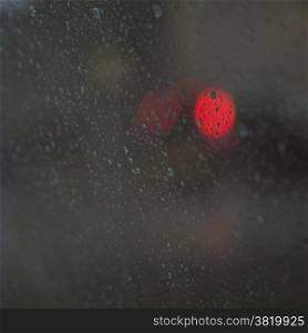 red lights of traffic seen through wet windshield during rainfall