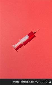 Red liquid serum or vaccine in plastic syringe 20 ml for an intravenous injection on a red background with hard shadow, copy space.. Disposable syringes of red blood or vaccine with shadows.