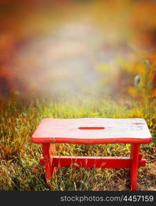 Red little wooden stool on autumn garden grass, nature background.