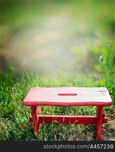Red little wooden stool on green grass lawn over garden nature background