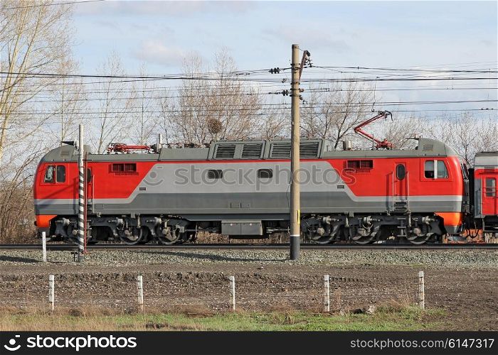 Red locomotive on electricity coming by rail.
