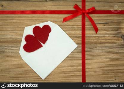 Red loop with hearts and white envelope on wooden background