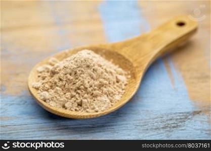 red maca root powder on a wooden spoon against painted wood