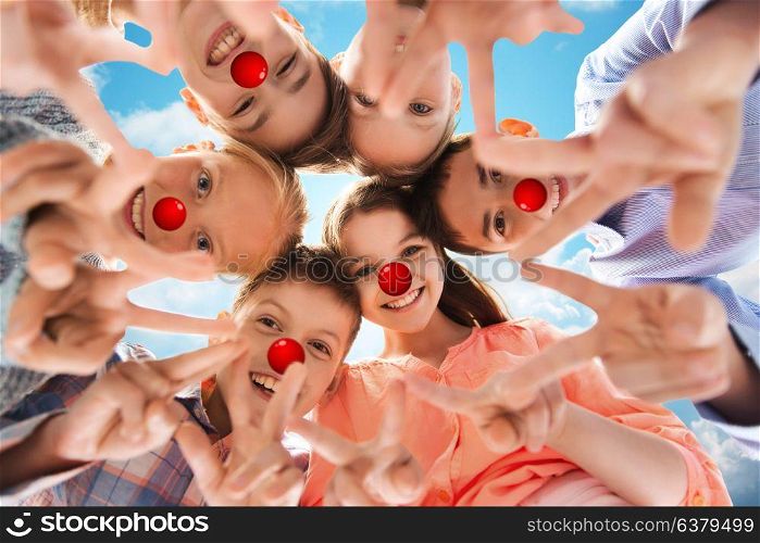 red nose day, charity and childhood concept - happy smiling children with clown noses showing peace hand sign and standing in circle over blue sky background. children showing peace hand sign at red nose day