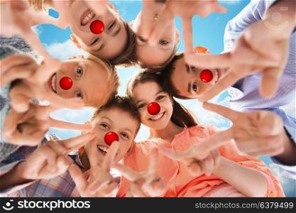 red nose day, charity and childhood concept - happy smiling children with clown noses showing peace hand sign and standing in circle over blue sky background. children showing peace hand sign at red nose day