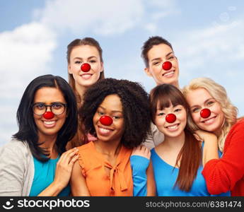 red nose day, diversity and people concept - international group of happy smiling different women with clown noses hugging over sky background. international group of happy women at red nose day